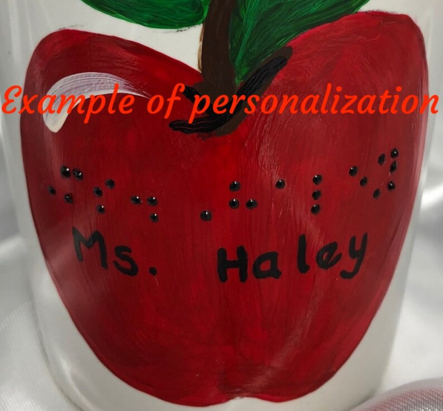 Apple design on other side of mug with example of personalization in braille and script