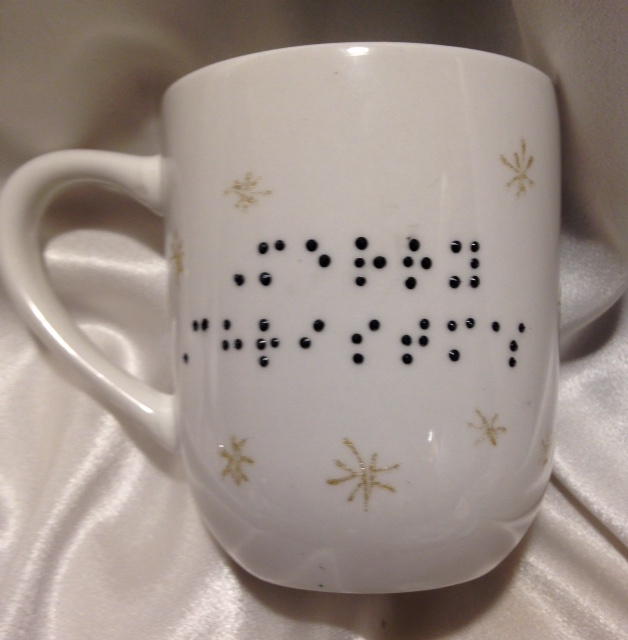 White ceramic mug with raised-dot braille "Merry Christmas" on one side, and green Christmas Tree on the other side.