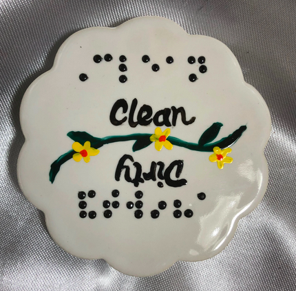 White ceramic shape with scalloped edges. Words in raised dot braille and script Clean and Dirty. 
