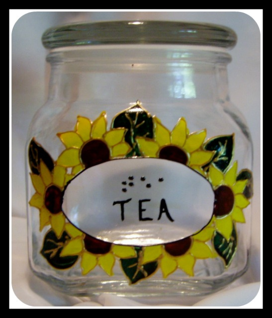 1 quart glass canister with lid. Shown canister for tea. Word in braille in script with yellow sunflowers around the word