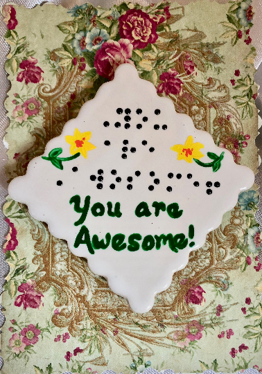 White ceramic magnet with words "You are Awesome" in braille and script, scalloped edges, with two yellow flowers with green stems and leaves