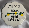 White ceramic shape with scalloped edges. Words in raised dot braille and script Clean and Dirty. 
